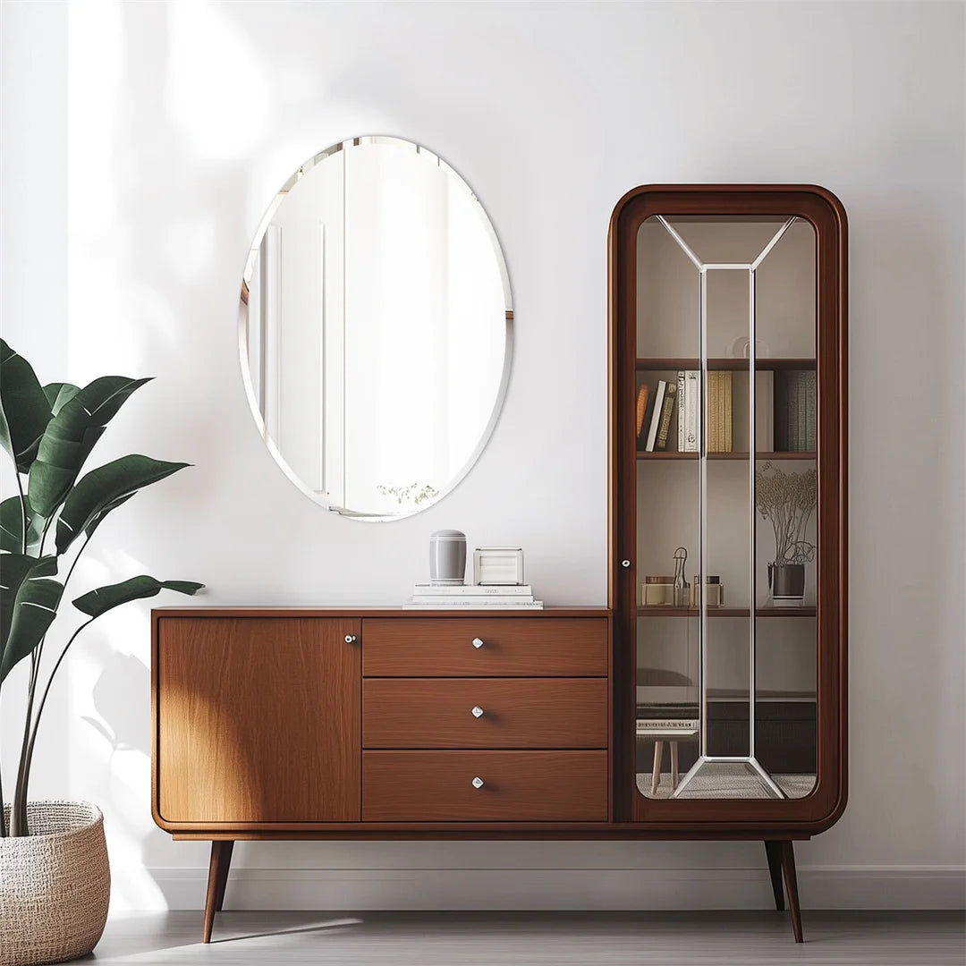 Meuble de rangement en bois avec un grand miroir ovale et une étagère en verre, situé dans un intérieur lumineux avec une plante verte.