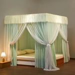 Lit à baldaquin en bois naturel avec rideaux blanc et vert clair suspendu au plafond, donnant une touche élégante et aérée à la chambre.