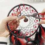 Capteur de rêves artisanal avec un motif en réseau décoré de perles rouges et de plumes noires.