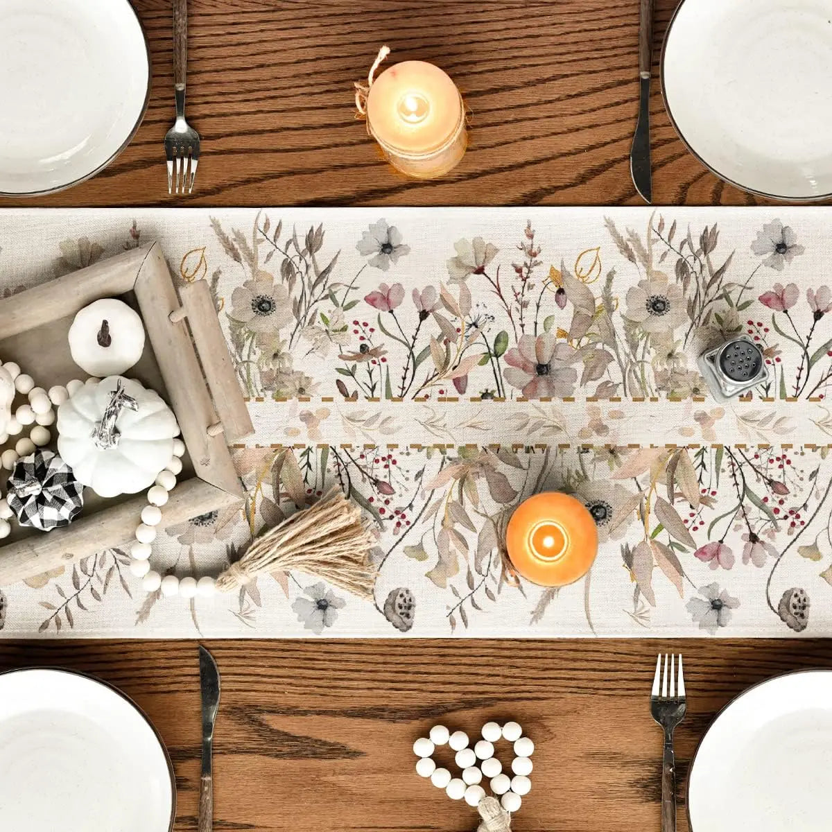 Une nappe en coton ornée de fleurs et de végétaux naturels, accompagnée de bougies et d'ustensiles de cuisine sur une table en bois.