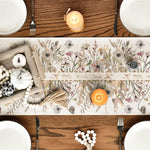 Une nappe en coton ornée de fleurs et de végétaux naturels, accompagnée de bougies et d'ustensiles de cuisine sur une table en bois.