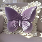 Coussin décoratif en forme de papillon violet, avec un motif élégant et délicat, posé sur un fond blanc texturé.