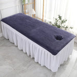 Une table de massage élégante avec une couverture pourpre et une bordure blanche, placée dans un environnement lumineux et harmonieux.