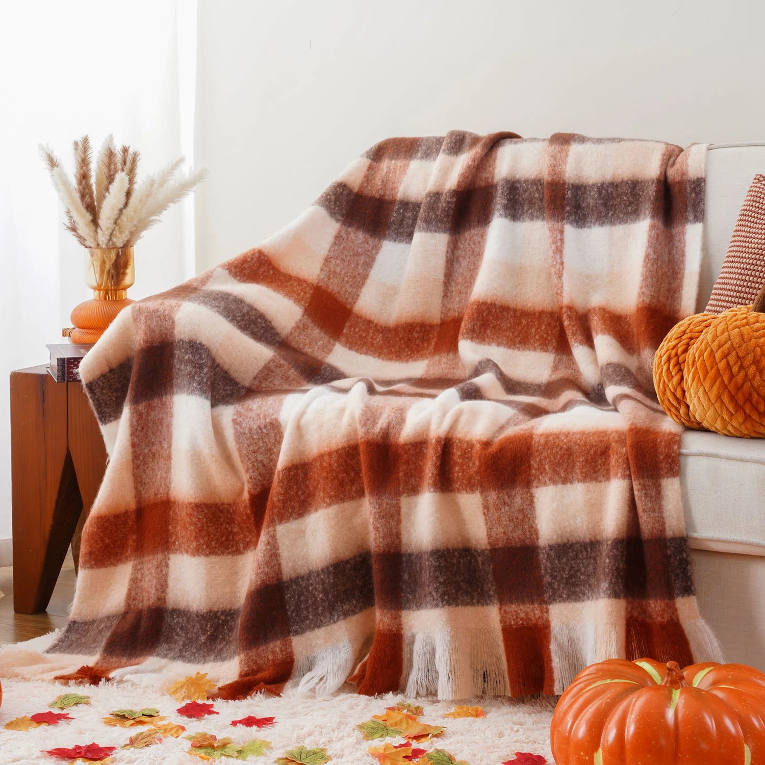 Un plaid à carreaux chauds et confortables, disposé sur un canapé avec des décorations d'automne, créant une ambiance cosy et accueillante.