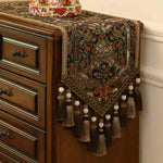 Élégante commode en bois foncé ornée d'un chemin de table aux motifs floraux et de pompes de couleurs vives, ainsi que de glands tressés ajoutant une touche de sophistication.