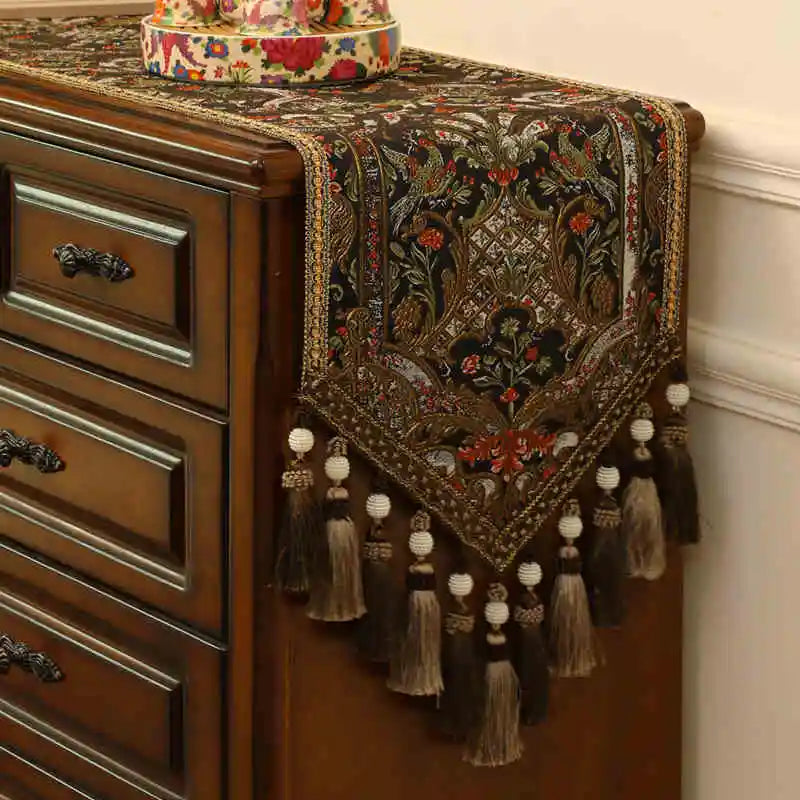 Élégante commode en bois foncé ornée d'un chemin de table aux motifs floraux et de pompes de couleurs vives, ainsi que de glands tressés ajoutant une touche de sophistication.