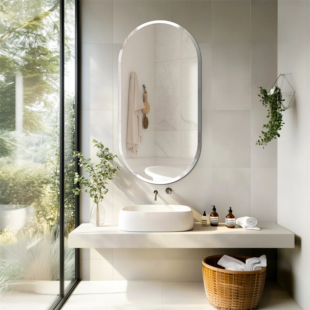 Un aménagement de salle de bain moderne et zen, avec une grande fenêtre offrant une vue sur la nature environnante, un lavabo en vasque blanche posé sur une surface de travail épurée, un miroir ovale lumineux et des accessoires de salle de bain à l'esthétique naturelle.