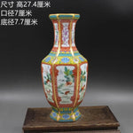 Vase de porcelaine décoré de motifs floraux et paysagers dans des tons rouge, bleu et vert, sur un support en bois.