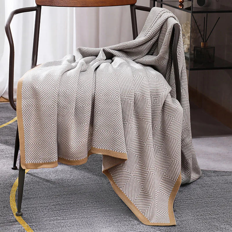 Couverture en laine gris foncé et blanc avec un motif géométrique décorative posée sur un fauteuil.