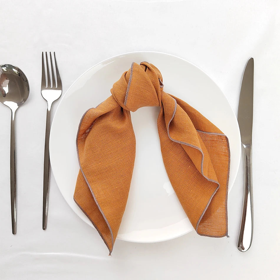 Un joli linge de table orange clair, posé sur une assiette blanche, accompagné d'une fourchette et d'un couteau en acier inoxydable.