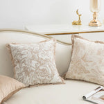 Deux oreillers décoratifs beige avec un motif floral sont posés sur un lit aux accents dorés.