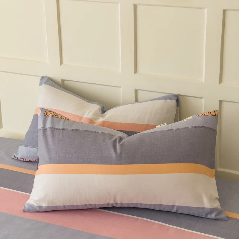 Des oreillers colorés et rayés dans des tons de gris, orange et rose, placés devant un mur de panneaux blancs, créant une ambiance douce et harmonieuse.