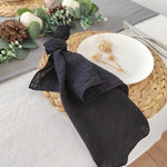 Serviette de table noire enroulée sur un set de table en tressage avec des décorations florales et des pommes de pin.