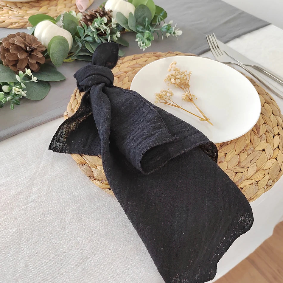 Serviette de table noire enroulée sur un set de table en tressage avec des décorations florales et des pommes de pin.