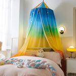Une chambre d'enfant lumineuse et colorée avec un lit à baldaquin aux tons dégradés de bleu, vert et jaune, surmonté d'étoiles scintillantes, entouré de coussins tressés pastel et de peluches.