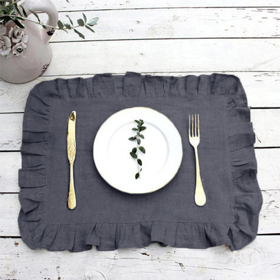 Une simple assiette blanche posée sur un napperon gris foncé, accompagnée d'une fourchette et d'un couteau dorés sur une table en bois blanc.