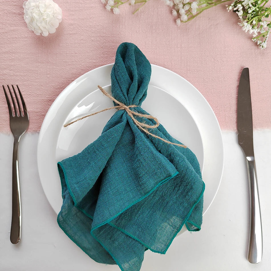 Une table de service élégante avec des serviettes de table turquoise élégamment pliées et attachées avec de la ficelle sur une assiette blanche, entourée de fleurs fraîches.