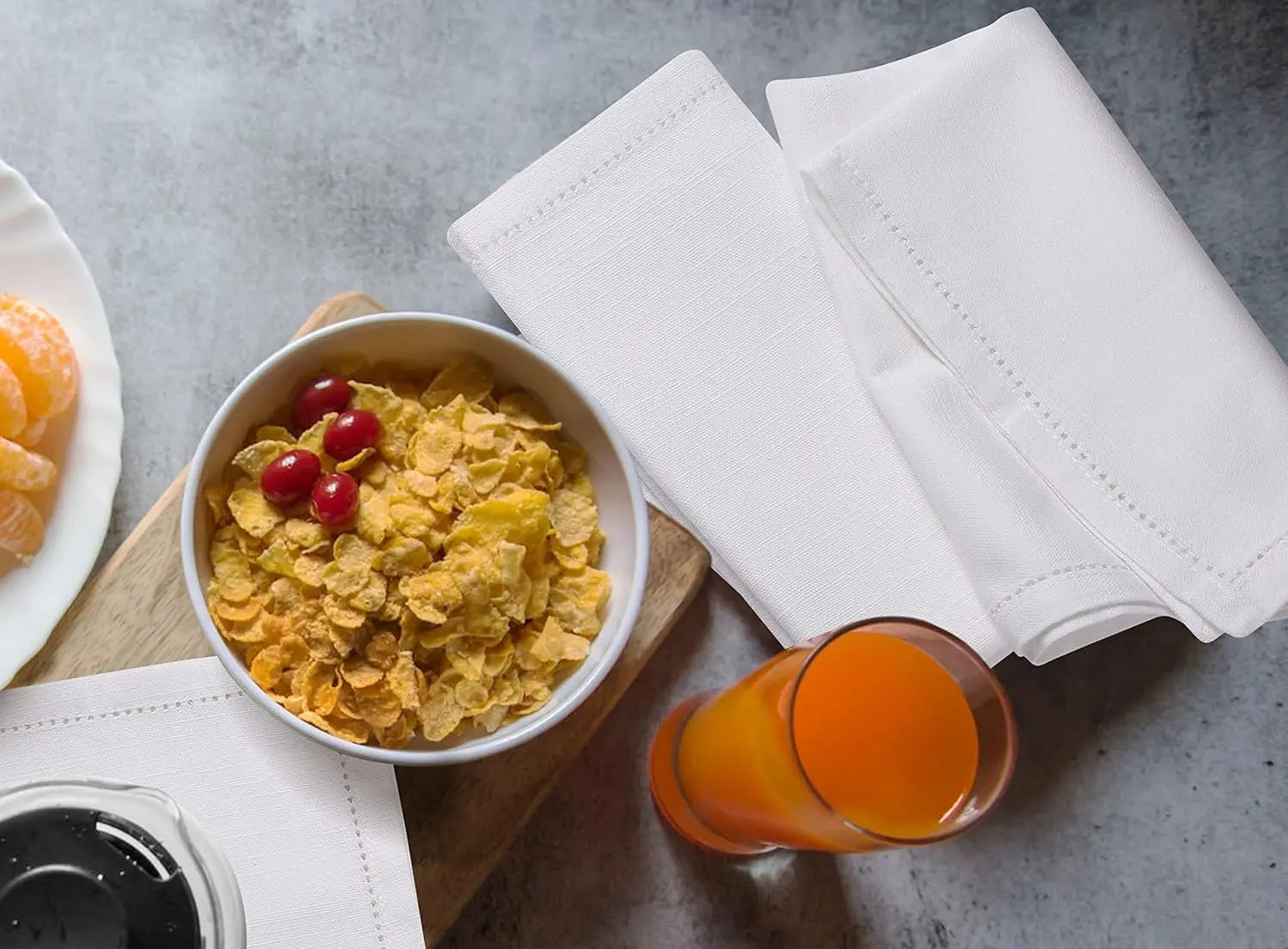 Une assiette de céréales dorées agrémentées de baies rouges, accompagnée d'un verre de jus d'orange, le tout posé sur une serviette blanche et un comptoir en pierre.