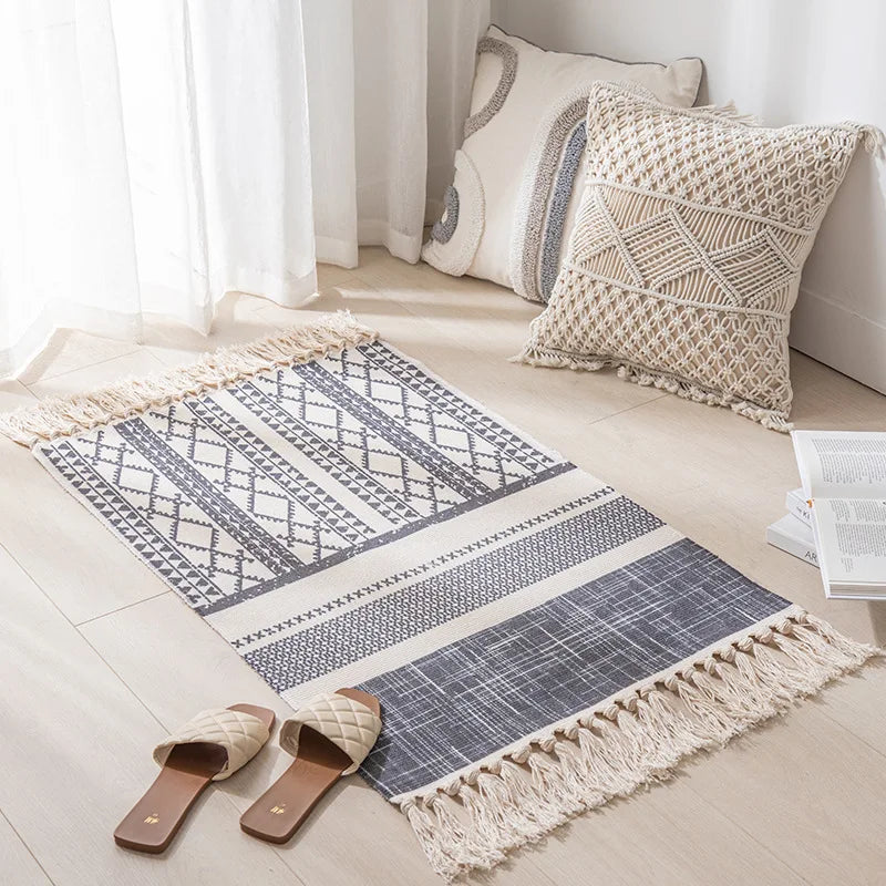 Tapis décoratif géométrique en macramé blanc et gris, avec des oreillers assortis, créant une ambiance chaleureuse et cocooning dans une pièce lumineuse.