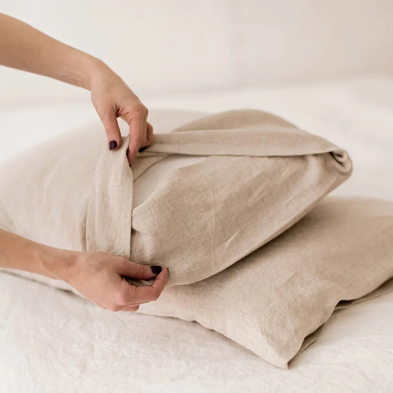 Une personne ajuste une housse de coussin en lin beige, reflétant le confort et la douceur des textiles de maison.