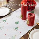 Nappe de table minimaliste avec motif d'arbres de Noël et points colorés, accompagnée de décorations rouges sur la table.