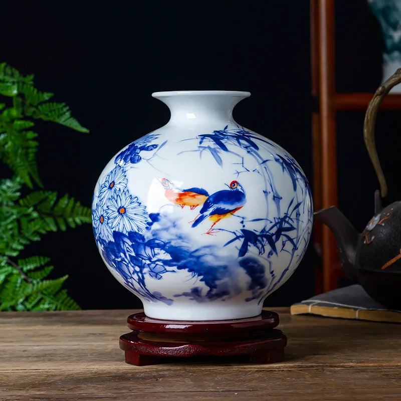 Un vase en porcelaine blanche décoré de motifs floraux bleus et de deux oiseaux colorés, reposant sur un support en bois.