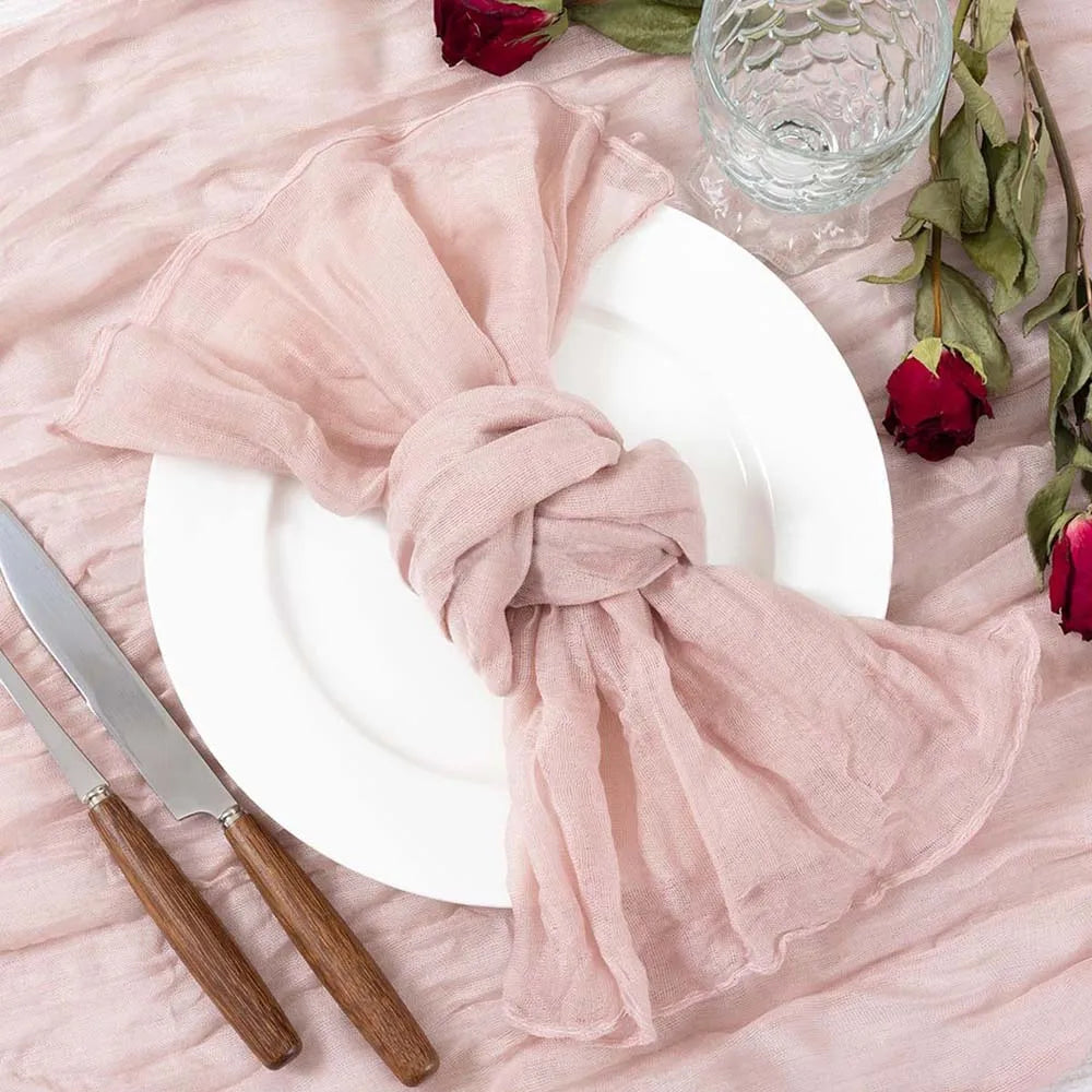Une table de dîner élégante avec des serviettes en tissu rose pastel, des roses rouges et de beaux couverts en bois.