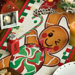 L'image représente des décorations et des aliments de Noël, comme un bonhomme en pain d'épice, des bonbons, une bougie et un cadre avec un paysage enneigé, reflétant l'esprit et l'ambiance festive de la saison.
