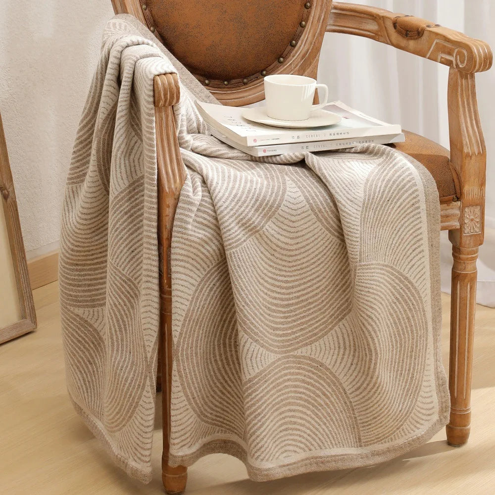 Une couverture douce et moelleuse, avec un motif de vagues subtil, posée sur un fauteuil en bois ancien, créant une atmosphère chaleureuse et confortable.