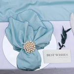 Un bouquet élégant de tissu vert avec un élégant épinglette de perles et de cristaux, posé sur une assiette blanche avec une carte de "Meilleurs voeux".