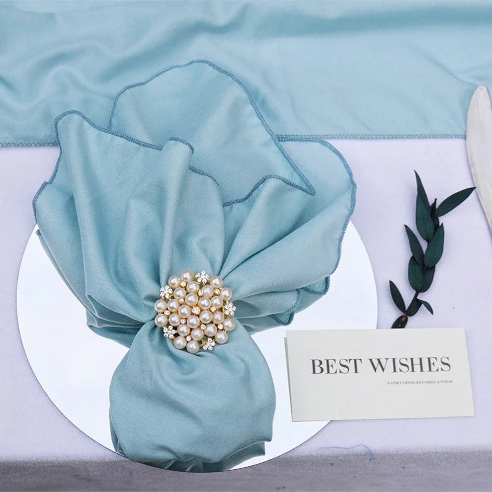 Un bouquet élégant de tissu vert avec un élégant épinglette de perles et de cristaux, posé sur une assiette blanche avec une carte de "Meilleurs voeux".