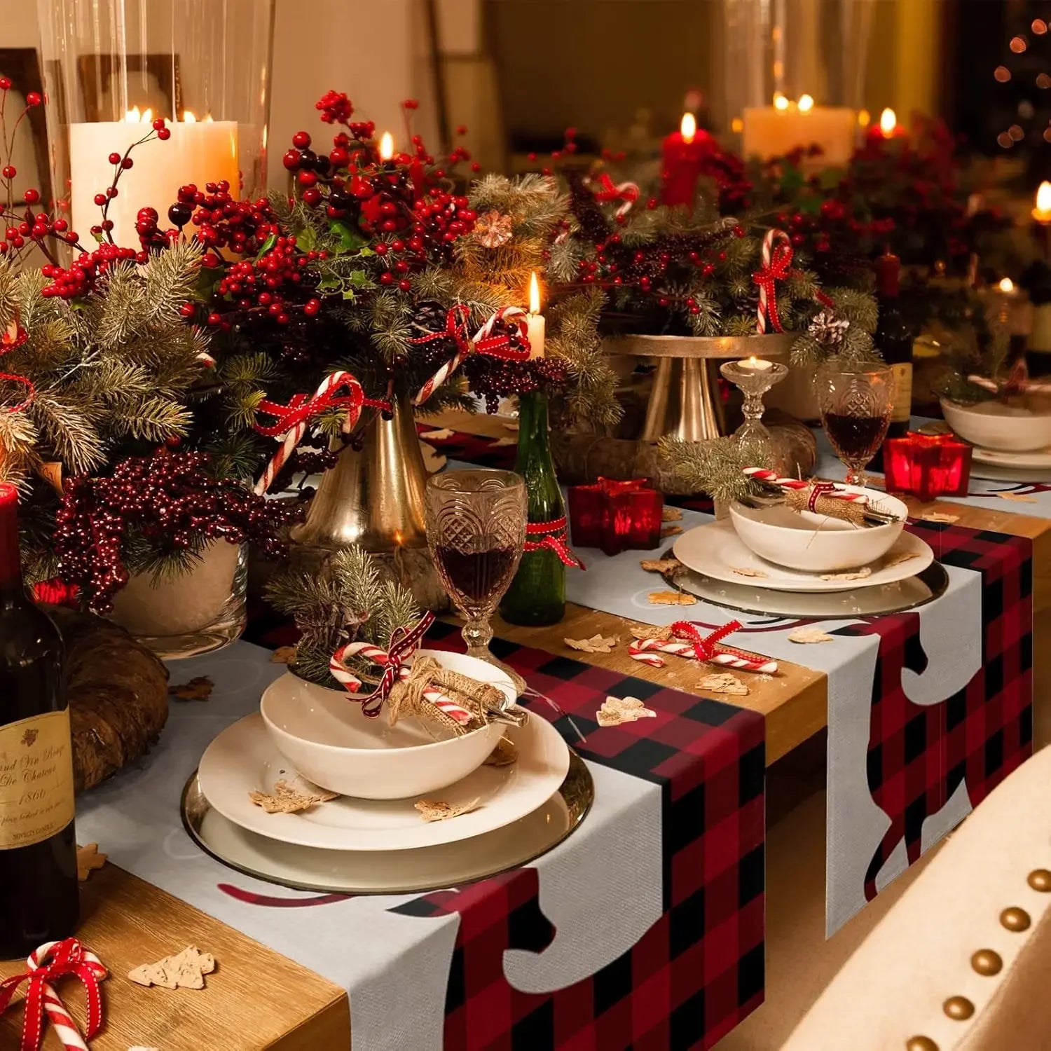 Une belle table de Noël décorée de branchages, de bougies allumées et de décorations rouges et dorées, créant une ambiance chaleureuse et festive.