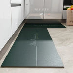 Tapis de bienvenue vert foncé avec logo et texte élégant sur un sol carrelé clair dans une cuisine moderne.