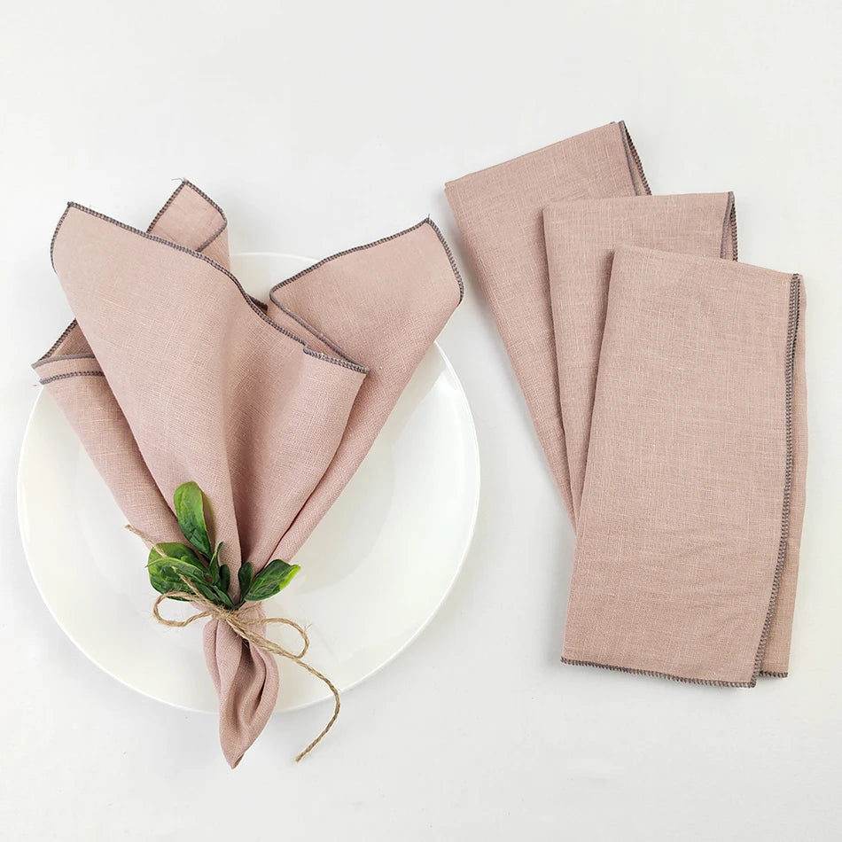 Serviettes en lin rose pâle posées sur une assiette blanche, décorées d'un lien en jute et de petites feuilles vertes.