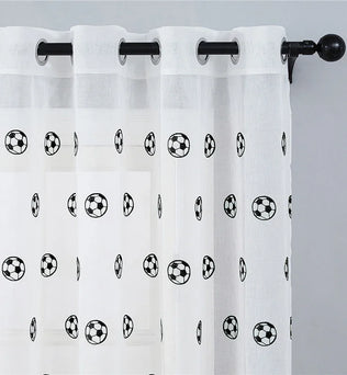 Voilage à motifs football suspendu sur une tringle noire, accroché à une fenêtre sur fond de mur gris.