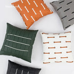 Cette image montre une variété de coussins décoratifs avec différents motifs géométriques et de textures en couleurs terre cuite, gris et vert.