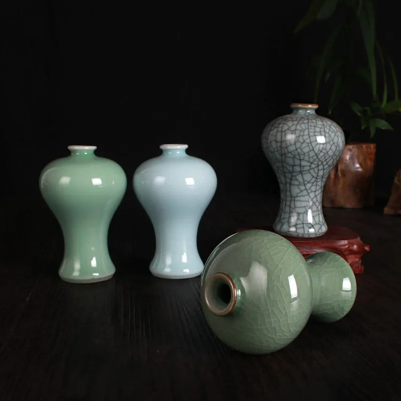 Assortiment de vases en céramique dans des teintes vertes et craquelées, avec un élément de décor en rouge-brun, sur un fond sombre.