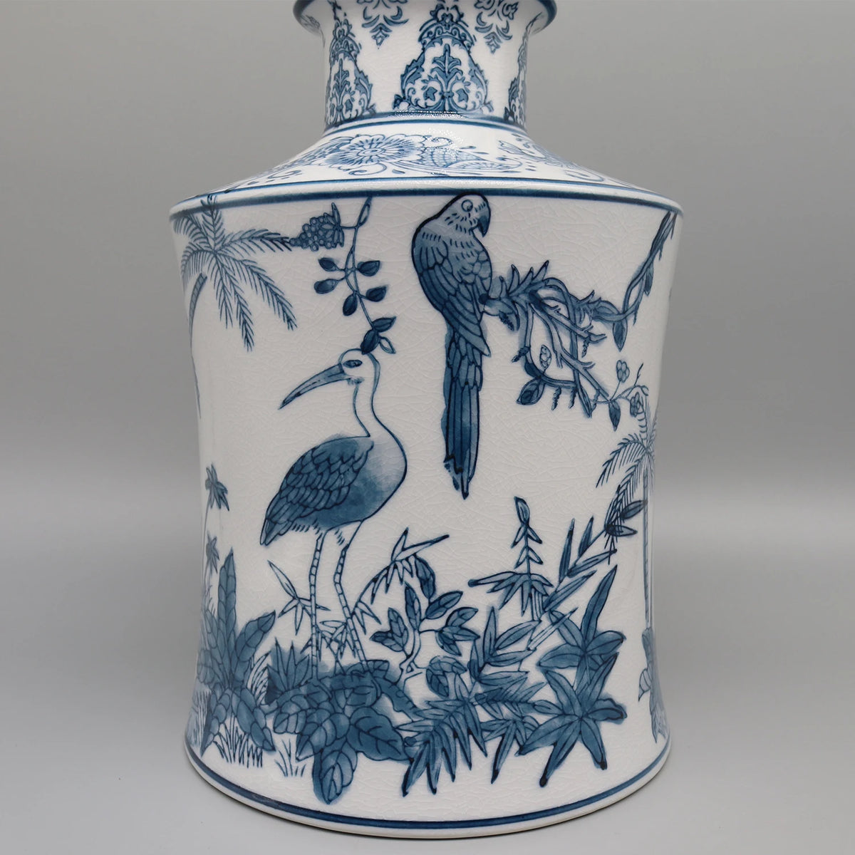 Un vase en porcelaine orné de motifs bleus et blancs représentant des oiseaux, des feuilles de palmier et une végétation luxuriante, créant une scène exotique et sophistiquée.
