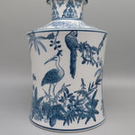 Un vase en porcelaine orné de motifs bleus et blancs représentant des oiseaux, des feuilles de palmier et une végétation luxuriante, créant une scène exotique et sophistiquée.