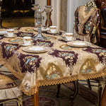 Une table élégante drapée d'une nappe richement ornée de motifs dorés et floraux, accompagnée de belles porcelaines et d'un impressionnant candélabre, créant une atmosphère luxueuse et raffinée.