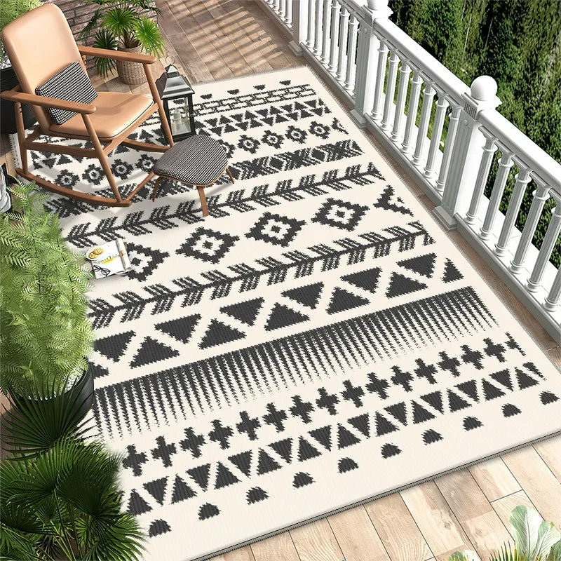 Tapis extérieur de style ethnique avec des motifs géométriques noirs et blancs sur une terrasse en bois, entouré de plantes vertes.