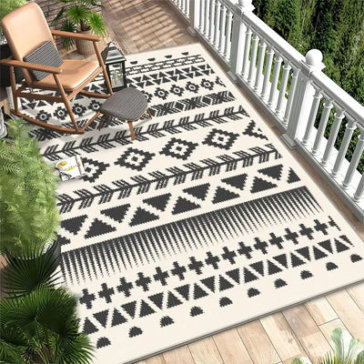 Tapis extérieur de style ethnique avec des motifs géométriques noirs et blancs sur une terrasse en bois, entouré de plantes vertes.