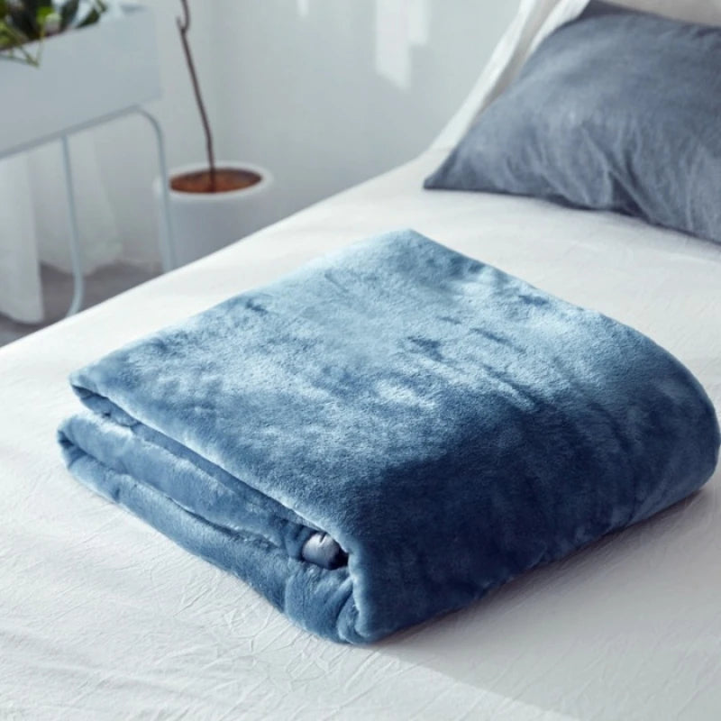 Couverture moelleuse et douillette de couleur bleue glacée, posée sur un lit blanc, créant une ambiance relaxante et cocooning.
