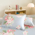 Chambre d'enfant avec coussins et linge de lit fleuris dans des tons pastel, étagère blanche avec décorations et livres.