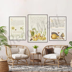 Cette pièce de style tropical présente trois œuvres encadrées mettant en scène des éléments naturels tels que des plantes et des fruits, complétés par des fauteuils en rotin et une décoration végétale.