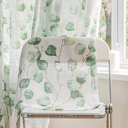 Voilage feuillage vert tombant élégamment sur une chaise blanche placée devant une fenêtre.