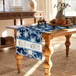 Une belle table en bois avec un chemin de table en motif de flocons de neige bleus et blancs, avec un message "Hello Winter" accentuant l'ambiance hivernale.
