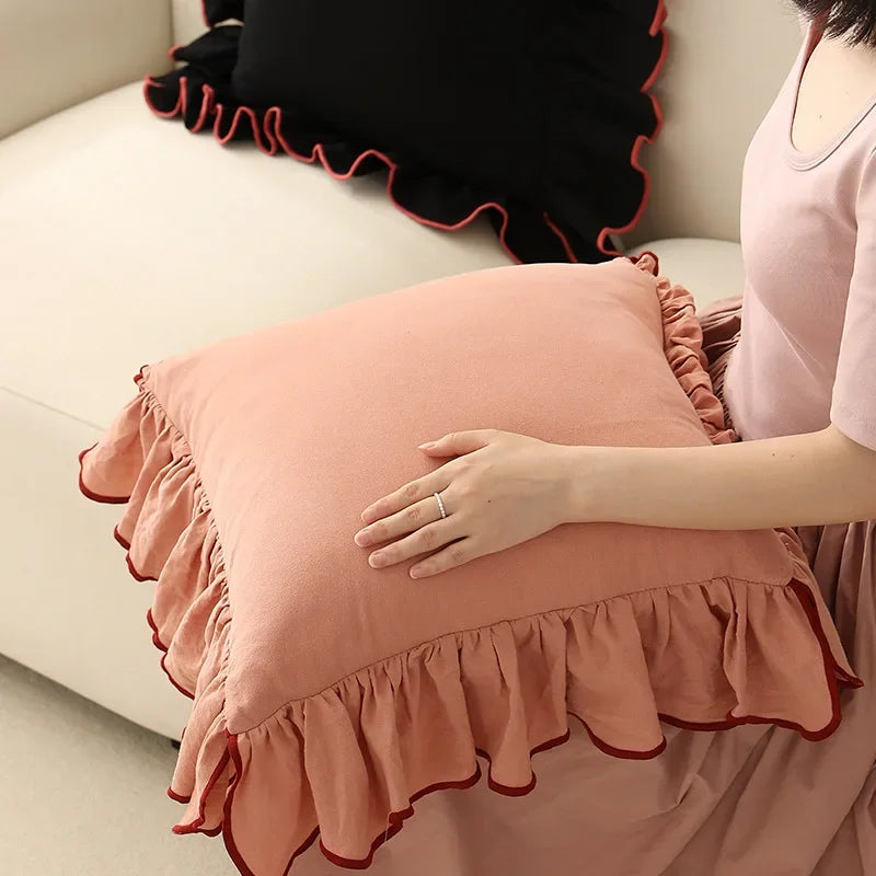 Coussin décoratif rose pâle avec dentelle ornementale, placé sur un canapé confortable.