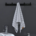 Une serviette de bain grise et blanche suspendue sur un porte-serviette noir, avec un lavabo blanc et un robinet en métal brillant.