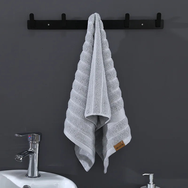 Une serviette de bain grise et blanche suspendue sur un porte-serviette noir, avec un lavabo blanc et un robinet en métal brillant.